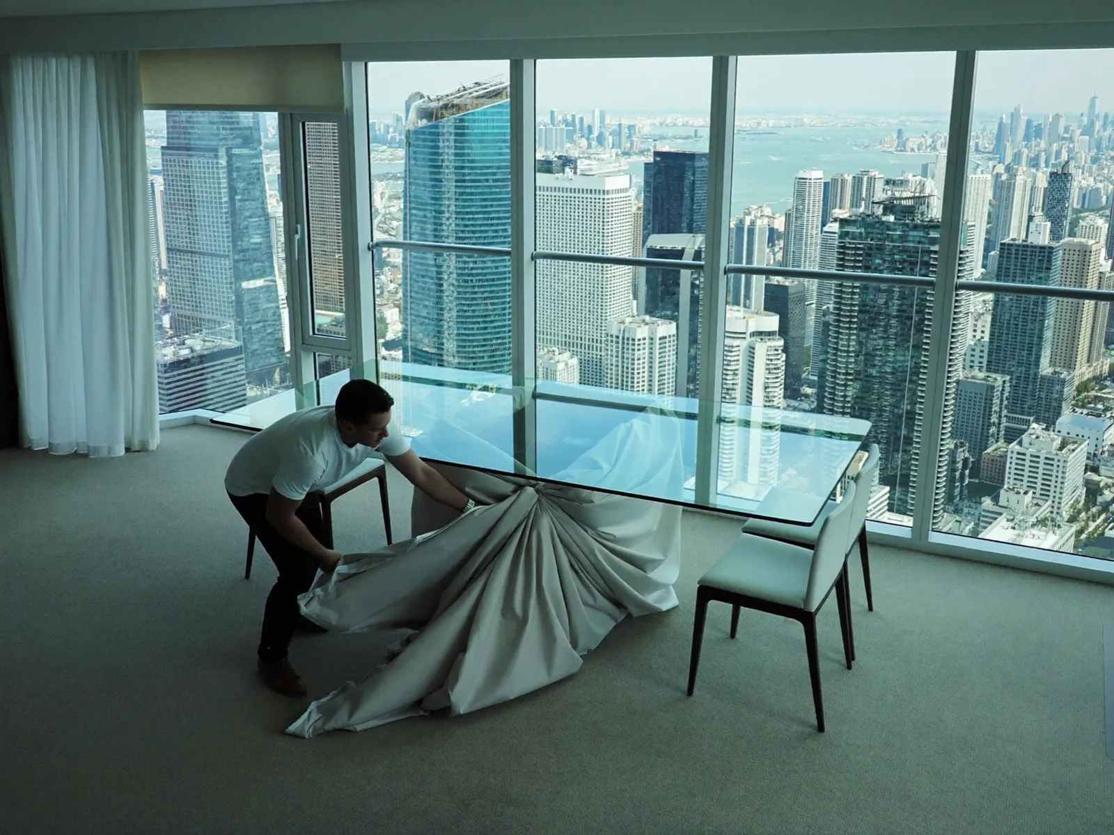 Mover wrapping a glass dining table in blankets beside floor-to-ceiling windows high above the Marina