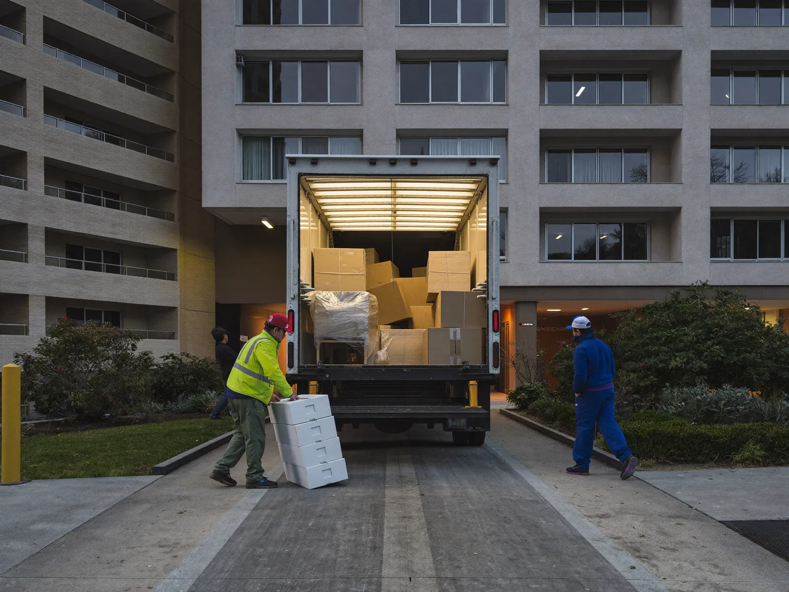 Crew loading wrapped furniture into a closed box truck at a tower basement loading bay